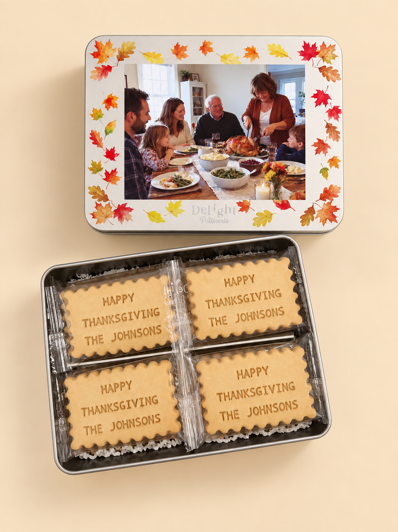A personalized Thanksgiving cookie tin set on a warm beige background. The top lid features colorful autumn leaves and a custom family photo in the center. The cookie tin holds the custom message shortbread with the message HAPPY THANKSGIVING THE JOHNSONS.